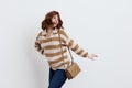 a joyful woman stands on a white background in a striped sweater and a bag on her shoulder , put her second hand on the