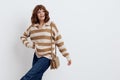 a joyful woman stands on a white background in a striped sweater and a bag on her shoulder , put her second hand on the