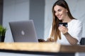 Joyful woman using laptop and credit card while sitting at home kitchen Royalty Free Stock Photo