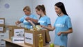 Joyful women in volunteer t-shirts putting food in boxes, provision donation