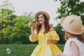 Joyful woman in yellow clothes play in park, rest and have fun with little cute child baby girl hold soap bubble blower Royalty Free Stock Photo