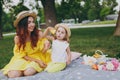 Joyful woman in yellow dress play on green grass in park, rest with little cute child baby girl hold soap bubble blower Royalty Free Stock Photo