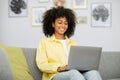 Joyful young african american woman working on laptop, sitting on sofa in home office, copy space. Royalty Free Stock Photo