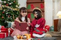 A joyful young Asian girl is reading a Christmas fairy tale story in a book to her younger sister Royalty Free Stock Photo