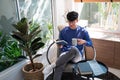 Joyful young Asian man in casual clothes and eyeglasses reading book while relaxing at living room of his home Royalty Free Stock Photo