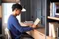 Joyful young Asian man in casual clothes and eyeglasses reading book while relaxing at living room of his home Royalty Free Stock Photo