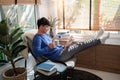 Joyful young Asian man in casual clothes and eyeglasses reading book while relaxing at living room of his home Royalty Free Stock Photo