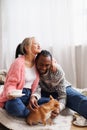 Joyful young asian woman holding coffee and hugging african american boyfriend with dog on bed Royalty Free Stock Photo