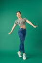 Joyful young Asian woman standing on one leg. Full length view of blissful girl dancing on green background