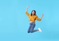 Joyful young asian woman in yellow shirt jumping and celebrating over blue background Royalty Free Stock Photo