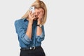 Joyful young attractive blonde woman in denim shirt talking on smart phone to her friend, looking cheerful and happy Royalty Free Stock Photo