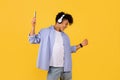 Young black guy enjoying music with headphones and smartphone on yellow backdrop Royalty Free Stock Photo