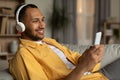 Joyful young black guy in headphones lying on couch and listening to music online on cellphone at home Royalty Free Stock Photo