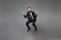 Joyful young business man in classic black suit shirt tie posing on grey background. Achievement career wealth