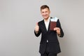 Joyful young business man in classic suit showing thumb up, holding passport, boarding pass ticket in hand isolated on