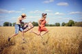 Joyful young couple having fun in wheat field. Excited man and woman running with retro leather suitcase on blue sky Royalty Free Stock Photo