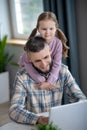 Joyful young dad, little daughter smiling looking at a laptop.