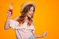Joyful young European female in summer straw hat, wears fashionable blouse, holds cold fresh cocktail, being in good mood, isolate