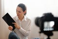 Joyful young girl recording video blog episode about new tech devices while sitting at home tablet and phone