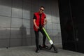 Joyful young hipster man in stylish red-black jeans clothes in sports sneakers in sunglasses with a vintage scooter stands Royalty Free Stock Photo