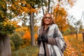 Joyful young hipster woman in a fashionable knitted scarf in stylish glasses in a trendy coat posing in a park outside the city. Royalty Free Stock Photo