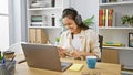 Joyful young hispanic woman worker having fun, dancing to music while working on her laptop at the office, exuding confidence Royalty Free Stock Photo