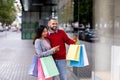 Joyful young interracial couple with gift bags looking at store window, checking mobile discount app near city mall Royalty Free Stock Photo