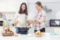 A joyful young lesbian pair in an apron cooks together in their home kitchen behind a wooden table with a frying pan and a spatula Royalty Free Stock Photo