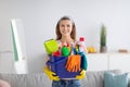 Joyful young maid holding bucket full of cleaning supplies at living room Royalty Free Stock Photo