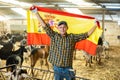 Joyful young male traveler waving Spanish flag during visit to livestock goat farm