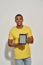 Joyful young man in casual yellow t shirt smiling at camera, showing digital tablet pc with blank screen while standing Royalty Free Stock Photo