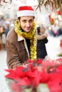 Joyful young man in Christmas hat looking flowers and Christmas toys at fair Royalty Free Stock Photo