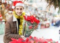 Joyful young man in Christmas hat looking flowers and Christmas toys at fair Royalty Free Stock Photo