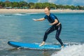 Joyful young woman beginner surfer with blue surf has fun on small sea waves. Active family lifestyle, people outdoor