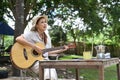 Joyful young woman playing guitar during camping alone near river bank on beautiful day Royalty Free Stock Photo