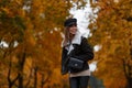 Joyful young woman in stylish outerwear in an elegant hat with a vintage bag stand in the park and enjoys the autumn scenery. Royalty Free Stock Photo