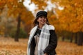 Joyful young woman in stylish outerwear in an elegant hat with a vintage scarf walks in the park and enjoys the autumn scenery. Royalty Free Stock Photo