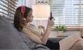 Joyful young woman wearing headphones and using smart phone on couch in cozy living room Royalty Free Stock Photo