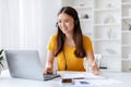 Joyful young woman wearing headset multitasking with pen and laptop at home Royalty Free Stock Photo