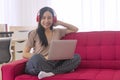 Woman wearing wireless headphones using laptop playlist listens music while sitting on red sofa at living room. Smile