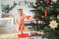 Joyfull little girl playing with Christmas ornament with a big smile on her face, walking past the Christmas tree