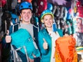 joyous couple of travelers at sports store, selects backpacks for camping