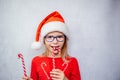 Happy little girl in eye glasses and Santa hat licking candy cane, Christmas child Ophthalmology