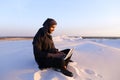 Educated Arab student uses laptop and works sitting on sand amid