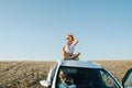 Joyous woman sitting on a car roof, enjoying wind and views on steppe plain