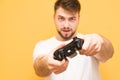 Joystick close-up and in focus. Concentrated gamer with a gamepad in hand, looking into the camera and playing video games on the