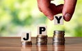 JPY Japan currency word symbol - business concept. Hands put wooden block on stacked increasing coin