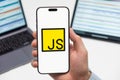 JS logo on the screen of smartphone in mans hand on the workplace background