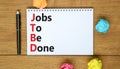 JTBD jobs to be done symbol. Concept words JTBD jobs to be done on white note on a beautiful wooden background. Businessman hand.