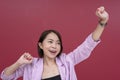 A jubilant short-haired young asian woman feels triumphant. Arms raised in the air. Studio shot with burgundy background